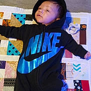Carmello joined the competition — help win amazing prizes! baby, infant, onesie, nike, hoodie, blue, black, quilt, patchwork, pacifier, floor, socks, child, lying_down, indoor, person, cute, young, soft_lighting, blanket