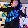 baby, infant, onesie, nike, hoodie, blue, black, quilt, patchwork, pacifier, floor, socks, child, lying_down, indoor, person, cute, young, soft_lighting, blanket