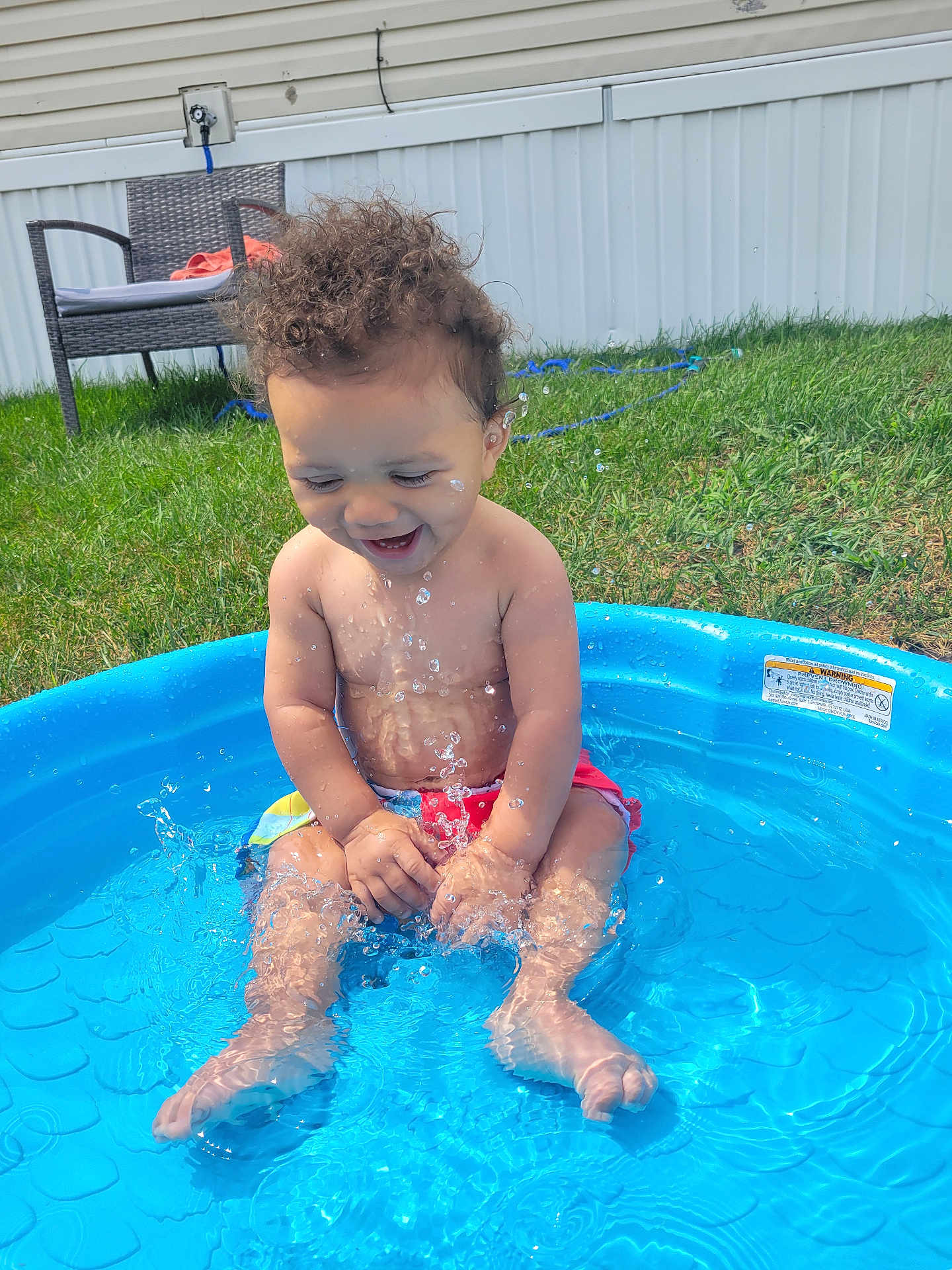 Carmello joined the competition — help win amazing prizes! toddler, child, water, pool, splashing, outdoor, grass, chair, smiling, happy, curly_hair, summer, sunny, bare_chest, playing, blue, plastic_pool, water_droplets, backyard, fun