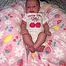baby, infant, onesie, pink_blanket, fruit_pattern, floral_pattern, cute, relaxed, indoor, person, newborn, soft_texture, footwear_bare, lying_down, child, sleepwear, decorative_blanket, small_hands, small_feet, expression