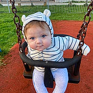 Kody joined the competition — help win amazing prizes! baby, child, swing, playground, hoodie, striped_clothing, cute, infant, outdoor, grass, red_surface, seat, chain, smiling, person, park, casual_wear, young_child, face, blue_eyes