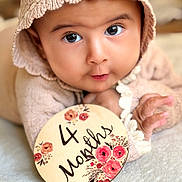 Hazel joined the competition — help win amazing prizes! baby, infant, 4_months, knitted_hat, sweater, milestone_sign, floral_design, blanket, close_up, portrait, cute, soft_focus, hand, lying_down, indoors, child, young_baby, face, curious, warm_lighting