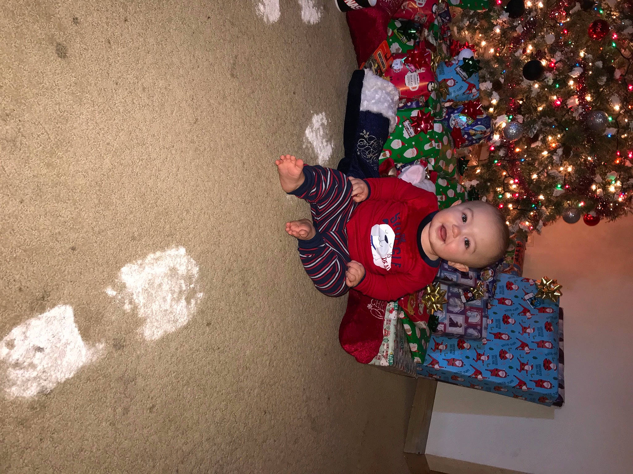 Gunner is registered to the contest to win money with this photo: baby, baby_toddler_clothing, carmine, christmas, christmas_decoration, christmas_eve, christmas_lights, christmas_ornament, christmas_tree, conifer, fictional_character, fir, holiday, holiday_ornament, interior_design, ornament, person, pine_family, sand, toddler