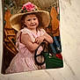 child, girl, hat, straw_hat, pink_dress, flower, rose, steering_wheel, wooden_fence, american_flag, portrait, vintage, indoor, smile, face, person, marble_surface, photograph, pose, cute