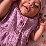 baby, infant, smiling, purple_clothing, headwrap, blanket, floral_pattern, cute, portrait, happy, skin, face, child, newborn, lying_down, buttoned_dress, indoors, soft_light, small_hands, peaceful