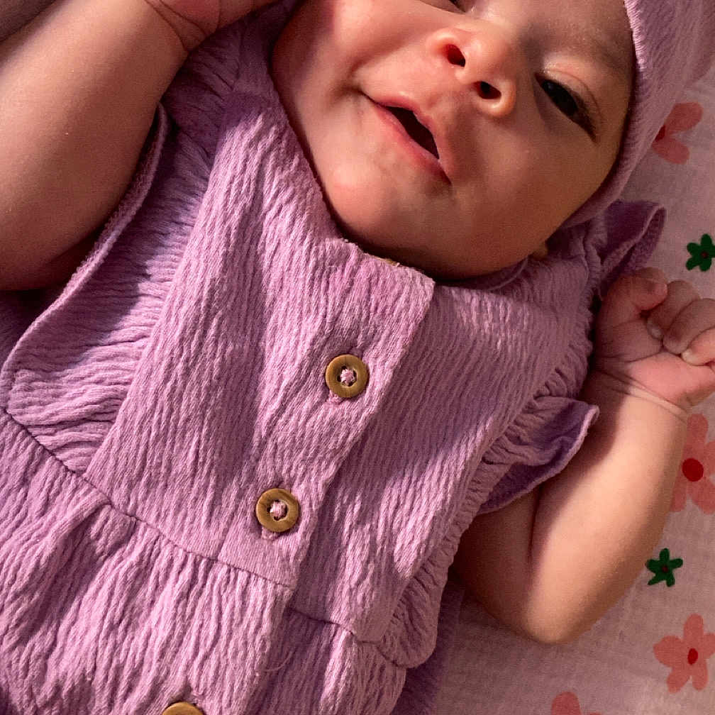 Chehla participe au concours pour gagner de l'argent avec cette photo : baby, blanket, buttoned_dress, child, cute, face, floral_pattern, happy, headwrap, indoors, infant, lying_down, newborn, peaceful, portrait, purple_clothing, skin, small_hands, smiling, soft_light