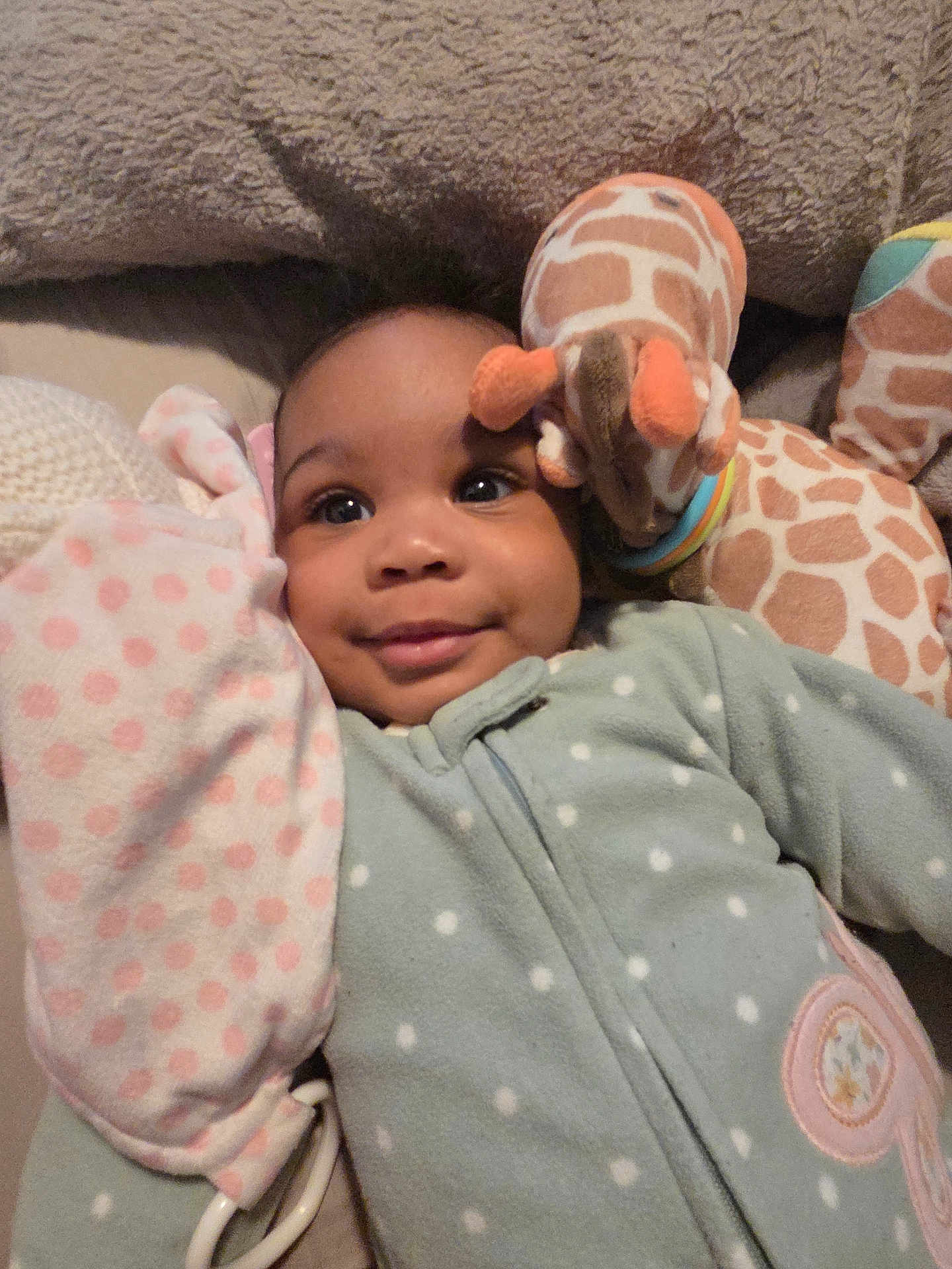 Kamora joined the competition — help win amazing prizes! baby, infant, smile, face, plush_toy, giraffe_toy, blanket, polka_dot, onesie, cozy, cute, child, soft_toy, lying_down, indoor, warm, comfort, happy, close_up, person