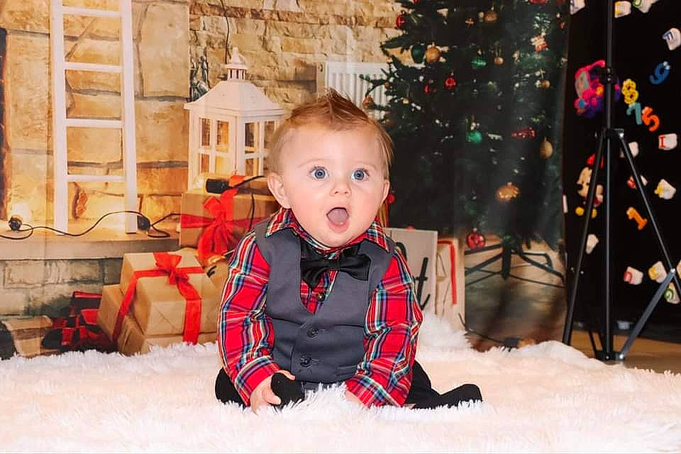 Drew is registered to the contest to win money with this photo: baby, baby_toddler_clothing, child, christmas, christmas_decoration, christmas_eve, christmas_lights, christmas_ornament, christmas_tree, conifer, holiday, holiday_ornament, home, interior_design, ornament, person, plaid, surprise, tartan, toddler
