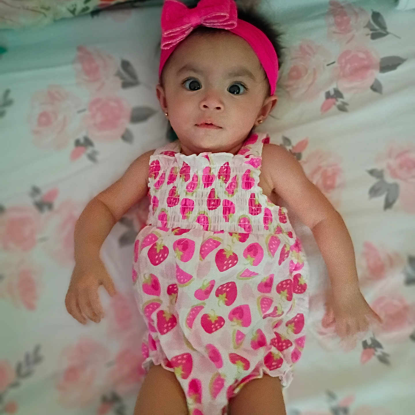Mia is registered to the contest to win money with this photo: adorable, baby, bow, child, curious_expression, cute, floral_bedspread, headband, indoors, infant, lying_down, person, pink, portrait, romper, skin, sleepwear, small_ears, soft_lighting, strawberry_pattern