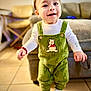 Basilio joined the competition — help win amazing prizes! toddler, child, green_overalls, winnie_the_pooh, indoor, smiling, white_shirt, white_shoes, floor_tiles, sofa, chair, furniture, happy, cute, baby, portrait, standing, person, home, cozy