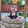 child, baby, one_year_old, crown, denim_overalls, outdoor, wooden_well, grass, picnic_table, fence, happy, curious, toddler, daylight, portrait, smiling, playful, young_child, nature, casual_clothing