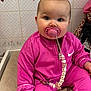 baby, pink_clothing, pacifier, indoor, heart_decor, tile_wall, cute, child, seated, soft_lighting, clothing, infant, person, face, hand, footwear, sock, pacifier_clip, expressionless, portrait