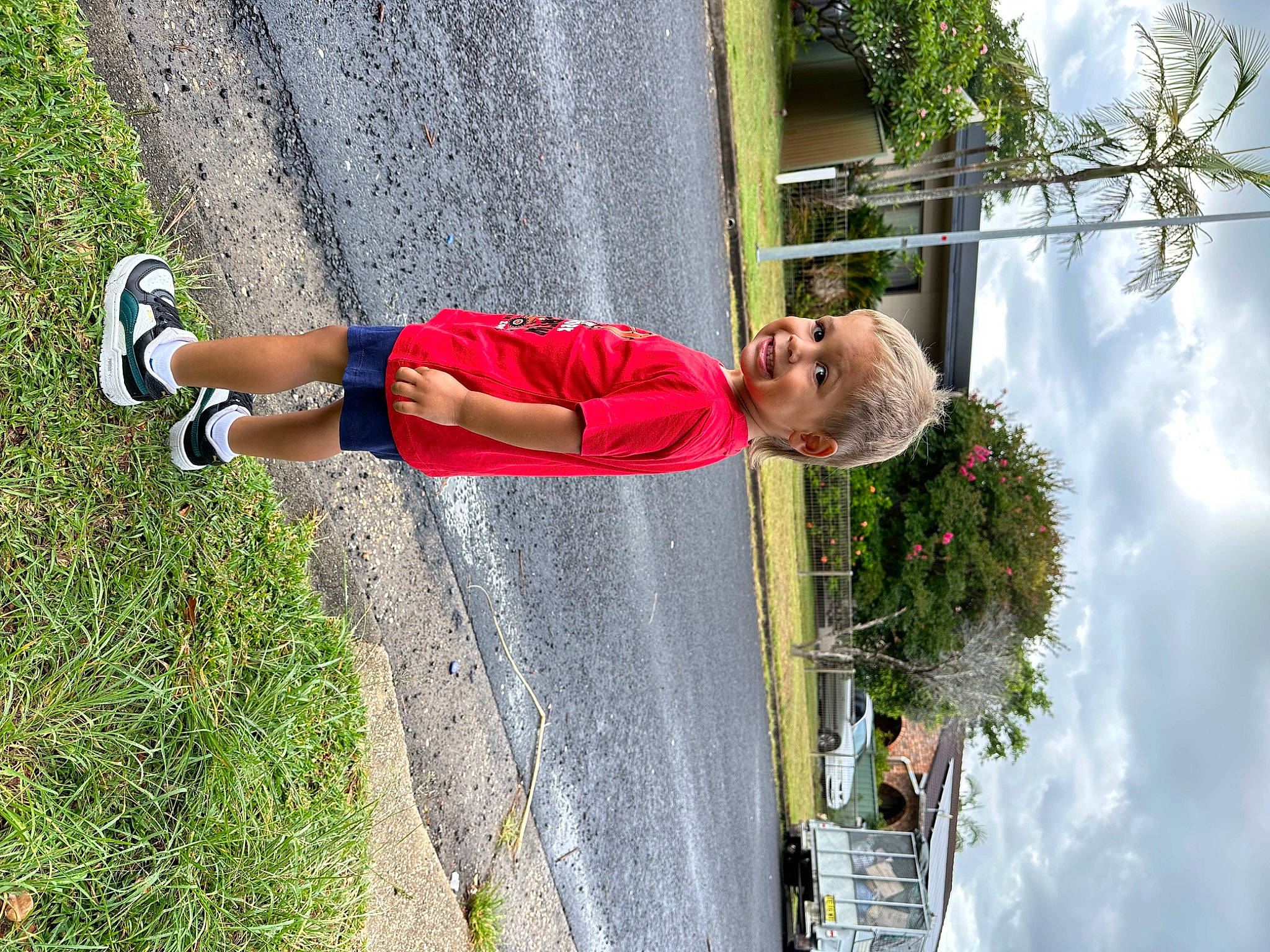 Tyler is registered to the contest to win money with this photo: asphalt, cloud, fun, grass, green, human_leg, joy, knee, leisure, people_in_nature, person, plant, pole, recreation, sidewalk, sky, smile, toddler, tree, walking_shoe