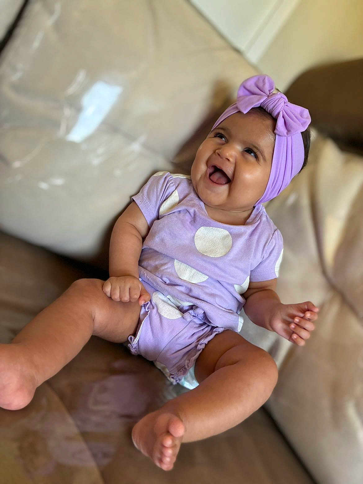 Eleizia a rejoint le concours — aidez-le/la à gagner de superbes lots ! baby, child, smiling, laughing, purple_clothing, headband, bow, couch, indoor, happy, cute, polka_dots, legs, feet, sitting, infant, person, portrait, fun, joy