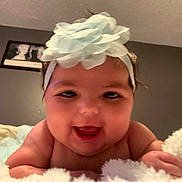 Nova is registered to the contest to win money with this photo: baby, infant, child, headband, flower, smile, chubby_cheeks, tongue, blanket, bed, bedroom, wall_art, closeup, portrait, face, eyes, hands, soft_texture, towel, cute