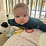 baby, infant, tummy_time, crib, wooden_slats, playmat, blanket, plush_toy, teether, toy_ring, cheeks, blue_eyes, face, indoor, tile_floor, caster_wheel, clothing, portrait, gaze, soft_texture