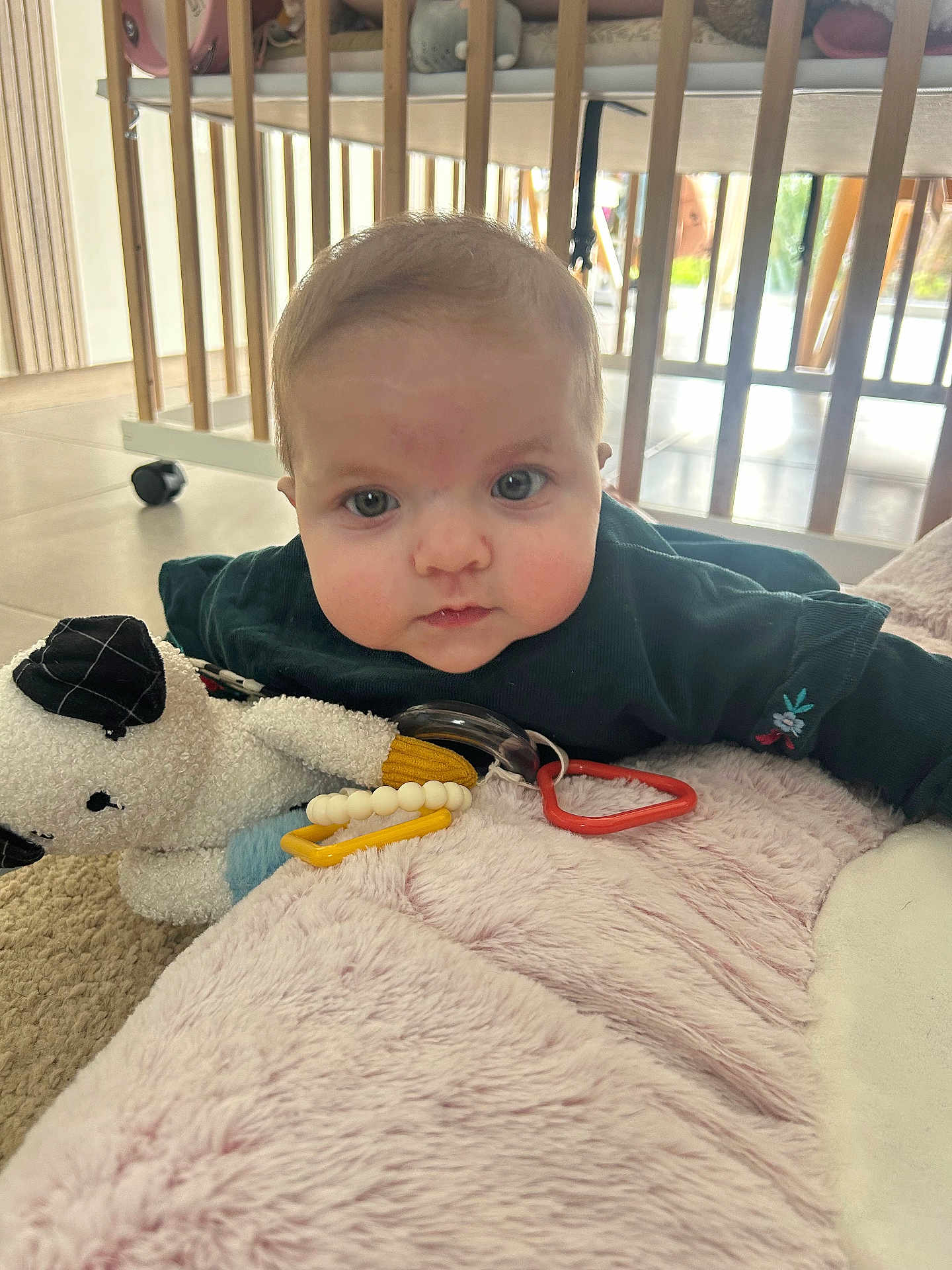 Constance participe au concours pour gagner de l'argent avec cette photo : baby, infant, tummy_time, crib, wooden_slats, playmat, blanket, plush_toy, teether, toy_ring, cheeks, blue_eyes, face, indoor, tile_floor, caster_wheel, clothing, portrait, gaze, soft_texture