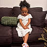calm, carpet, child, couch, crossed_legs, curly_hair, cute, decor, furniture, girl, home, indoor, living_room, looking_down, pillow, portrait, shoes, sitting, table, white_dress