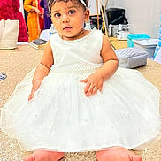 Kaylin Leora is registered to the contest to win money with this photo: baby, child, dress, white_dress, headband, bow, barefoot, sitting, sparkly_surface, indoor, people_in_background, curious, portrait, cute, child_fashion, celebration, floor, person, face, event