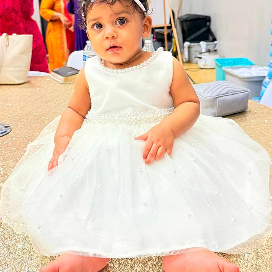 Kaylin Leora is registered to the contest to win money with this photo: baby, child, dress, white_dress, headband, bow, barefoot, sitting, sparkly_surface, indoor, people_in_background, curious, portrait, cute, child_fashion, celebration, floor, person, face, event
