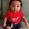 baby, child, curly_hair, red_shirt, fourth_of_july, navy_shorts, couch, green_couch, texture, sitting, portrait, indoors, cute, wide_eyes, expression, infant, person, clothing, casual, young