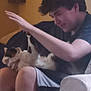 person, cat, calico_cat, couch, indoor, sitting, arm, hand, furniture, wall, shelf, shorts, black_shirt, pet, domestic_animal, relaxing, home, casual, young_adult, interaction
