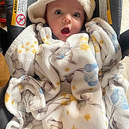Colton is registered to the contest to win money with this photo: baby, infant, child, portrait, wide_eyed, surprised, open_mouth, hat, blanket, bundled, infant_carrier, seated, indoor, cozy, textile, patterned_blanket, face, eyes, photograph, safe