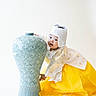 toddler, child, hanbok, traditional_clothing, yellow_skirt, white_hat, ceramic_vase, blue_vase, ornate, patterned, portrait, cute, playful, studio_shot, white_background, asian_child, cultural, smiling, young_child, celebration