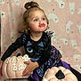 toddler, child, girl, pumpkin, halloween, costume, black_dress, purple_skirt, ghost_pattern, background, blue_eyes, curly_hair, top_bun, pouting, sitting, holiday, decor, cute, playful, indoor