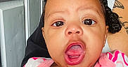 Emonnie is registered to the contest to win money with this photo: baby, child, infant, portrait, close_up, face, wide_eyed, open_mouth, expression, smiling, pink_clothing, onesie, braids, adult, caregiver, indoor, door, doorway, tattoo, photography