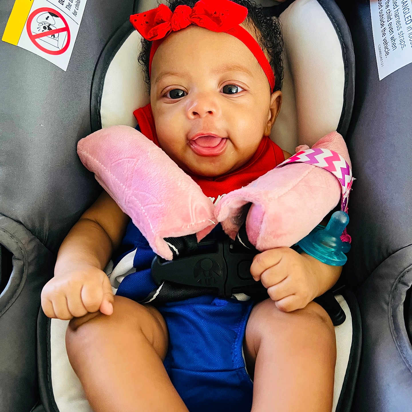 Emonnie is registered to the contest to win money with this photo: baby, infant, child, car_seat, red_headband, bow, smiling, tongue_out, portrait, indoors, pink_blanket, plush_toy, pacifier, blue_clothing, safety_harness, curly_hair, sitting, close_up, happy, photography