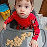 toddler, child, high_chair, pajamas, red_clothing, food, pasta, kitchen, floor, plastic_tray, face, eyes, hand, indoor, young_child, cute, expression, sitting, meal_time, table