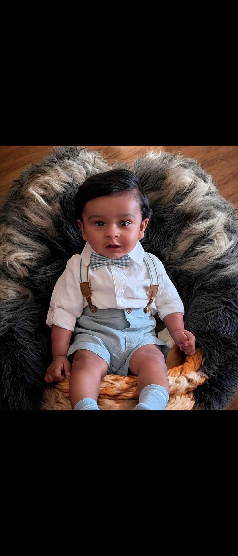 Dylan is registered to the contest to win money with this photo: baby, child, infant, boy, face, smile, clothing, bow_tie, suspenders, sitting, cushion, fur, soft_texture, indoors, portrait, cute, happy, looking_at_camera, shorts, socks