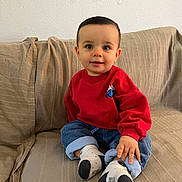 Mylan a rejoint le concours — aidez-le/la à gagner de superbes lots ! toddler, child, baby, sitting, couch, red_sweater, blue_jeans, socks, smiling, indoors, cute, portrait, young_child, casual_clothing, happy, face, hand, feet, home, comfortable