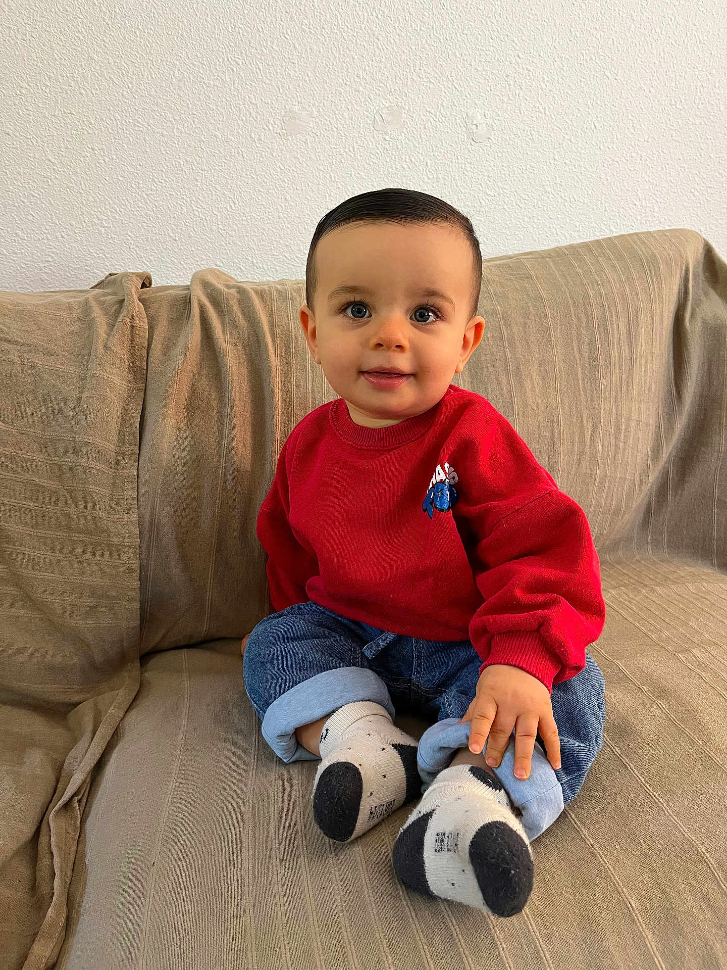 Mylan a rejoint le concours — aidez-le/la à gagner de superbes lots ! toddler, child, baby, sitting, couch, red_sweater, blue_jeans, socks, smiling, indoors, cute, portrait, young_child, casual_clothing, happy, face, hand, feet, home, comfortable