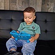 Zehian is registered to the contest to win money with this photo: toddler, child, tablet, blue, couch, black, leather, wooden_wall, indoor, casual_clothing, sneakers, short_hair, focused, sitting, technology, playful, relaxed, modern, cute, smiling