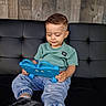 toddler, child, tablet, blue, couch, black, leather, wooden_wall, indoor, casual_clothing, sneakers, short_hair, focused, sitting, technology, playful, relaxed, modern, cute, smiling