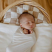 Isaac is registered to the contest to win money with this photo: newborn, baby, sleeping, swaddled, blanket, basket, cushion, wooden_floor, infant, peaceful, cozy, resting, indoors, portrait, head, face, child, soft_lighting, wrapped, quiet
