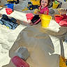 child, children, sand, sandbox, toys, buckets, shovels, toy_trucks, smiling, curly_hair, play, indoor, yellow_bucket, red_bucket, plastic_toys, happy, playing, casual_clothing, multiracial_children, daylight