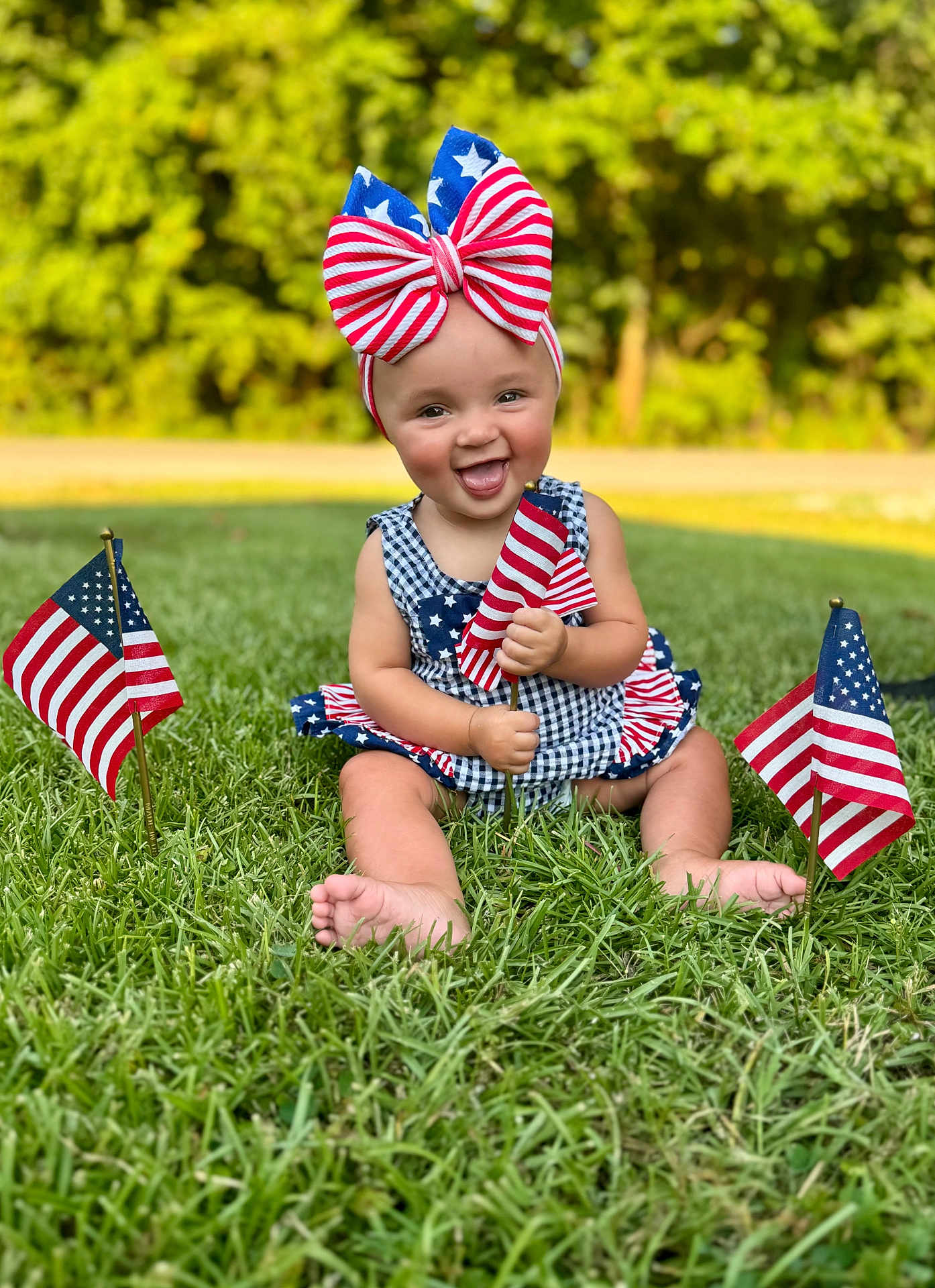 Oaklee is registered to the contest to win money with this photo: baby, child, grass, outdoor, flag, american_flag, headband, bow, smile, happy, patriotic, summer, nature, person, sitting, greenery, cute, celebration, holiday, dress
