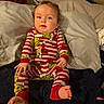 baby, child, pajamas, bed, pillow, foot, hand, face, blue_eyes, red, white, green, striped_clothing, indoors, curly_hair, person, sleepwear, sitting, cute, infant