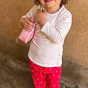 Lya participe au concours pour gagner de l'argent avec cette photo : child, toddler, girl, sunglasses, curly_hair, smile, white_top, pink_purse, pink_pants, white_sneakers, standing, outdoor, textured_wall, playful, portrait, accessory, cute, happy, reflection, shoes