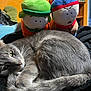 cat, gray_cat, plush_toy, stuffed_animal, bedroom, blanket, indoor, relaxed, cozy, feline, pet, toy, orange_wall, furniture, curious, sleepy, whiskers, tail, resting, soft