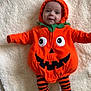 Ezio participe au concours pour gagner de l'argent avec cette photo : baby, infant, costume, pumpkin, orange, striped_socks, blanket, cute, smiling, face, hood, child, lying_down, soft_texture, playful, holiday, halloween, warm_clothing, indoors, adorable