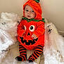baby, pumpkin_costume, halloween, orange, black_stripes, striped_tights, spiders, cobwebs, costume, cute, child, indoor, holiday, festive, sitting, portrait, face, hooded_outfit, soft_texture, seasonal