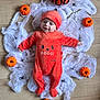 baby, infant, halloween, pumpkin, costume, orange_clothing, hat, spider_web, toy_pumpkin, floor, decorations, smiling, cute, festive, holiday, child, person, lying_down, indoor, celebration
