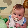 Lilah is registered to the contest to win money with this photo: baby, pacifier, blue_eyes, plastic_balls, green_balls, light_green_balls, bib, blue_clothing, child, indoor, play_area, face, portrait, infant, cute, curious, soft_background, animal_wall_art, hand, skin