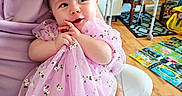 Lilah is registered to the contest to win money with this photo: baby, child, adult, holding, pink_dress, floral_pattern, indoor, living_room, walker, wooden_floor, play_mat, chair, tattoo, curious, affection, clothing, portrait, person, smiling, seated