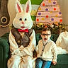 child, boy, glasses, easter_bunny, costume, couch, green_couch, easter_eggs, wooden_eggs, holiday, indoor, decorations, clock, vintage_clock, vest, bow_tie, white_fur, smiling, festive, casual_clothing