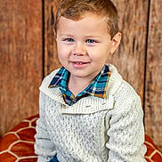 Ashton joined the competition — help win amazing prizes! child, boy, smiling, sitting, sweater, plaid_shirt, cushion, blue_pants, face, portrait, indoor, decor, bunting_flags, wooden_background, cozy, happy, casual_clothing, young, cute, knitwear